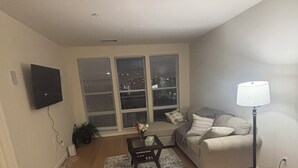 A living room with a sofa, a coffee table, a lamp, and a TV mounted on the wall.