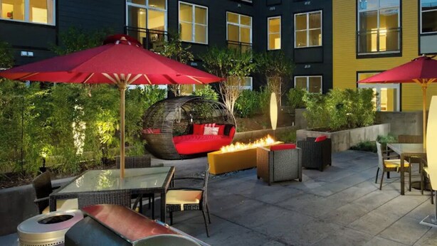 An outdoor patio area with seating and a fire feature, surrounded by buildings with illuminated windows.
