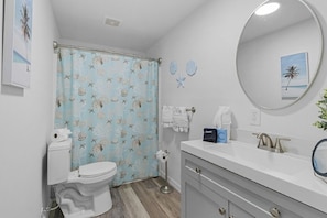 Een badkamer met toilet, douchegordijn, wastafel en spiegel.