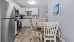 A compact kitchen with white cabinets, a stainless steel refrigerator, and a dining area with a wooden table and chairs. - LOCATION!  LOCATION!   Charming 2-bedroom house in delightful Fort Myers Beach (Fort Myers Beach)