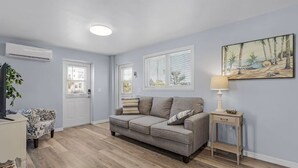 A living room with a grey sofa, a small side table, a lamp, and a painting on the wall. - LOCATION!  LOCATION!   Charming 2-bedroom house in delightful Fort Myers Beach (Fort Myers Beach)