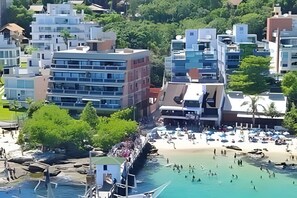 A coastal hotel with multiple floors, a beach in the background, and a rocky shoreline. - Borboleta do Mar (Bombinhas)