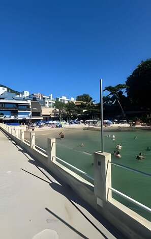 A coastal area with a beach, a promenade, and buildings in the background. - Borboleta do Mar (Bombinhas)