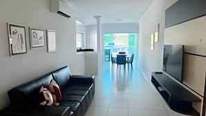 Ein modernes Wohnzimmer mit einer schwarzen Couch, einem Flachbildfernseher und einem Essbereich mit Tisch und Stühlen.