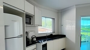 Eine moderne Küche mit weißen Schränken, einer schwarzen Arbeitsplatte und Blick auf eine grüne Landschaft durch die Fenster.