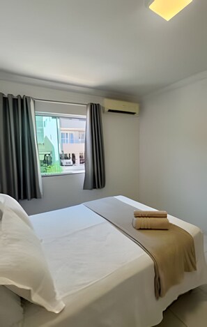 A hotel room with two beds, a window with curtains, an air conditioning unit, and a view of buildings outside. - Borboleta do Mar (Bombinhas)