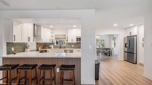A modern kitchen with white cabinetry, a central island with stools, and a stainless steel refrigerator. - Modern Waterfront Home w/ Pool Near Airport & South Tampa Hotspots (Tampa)
