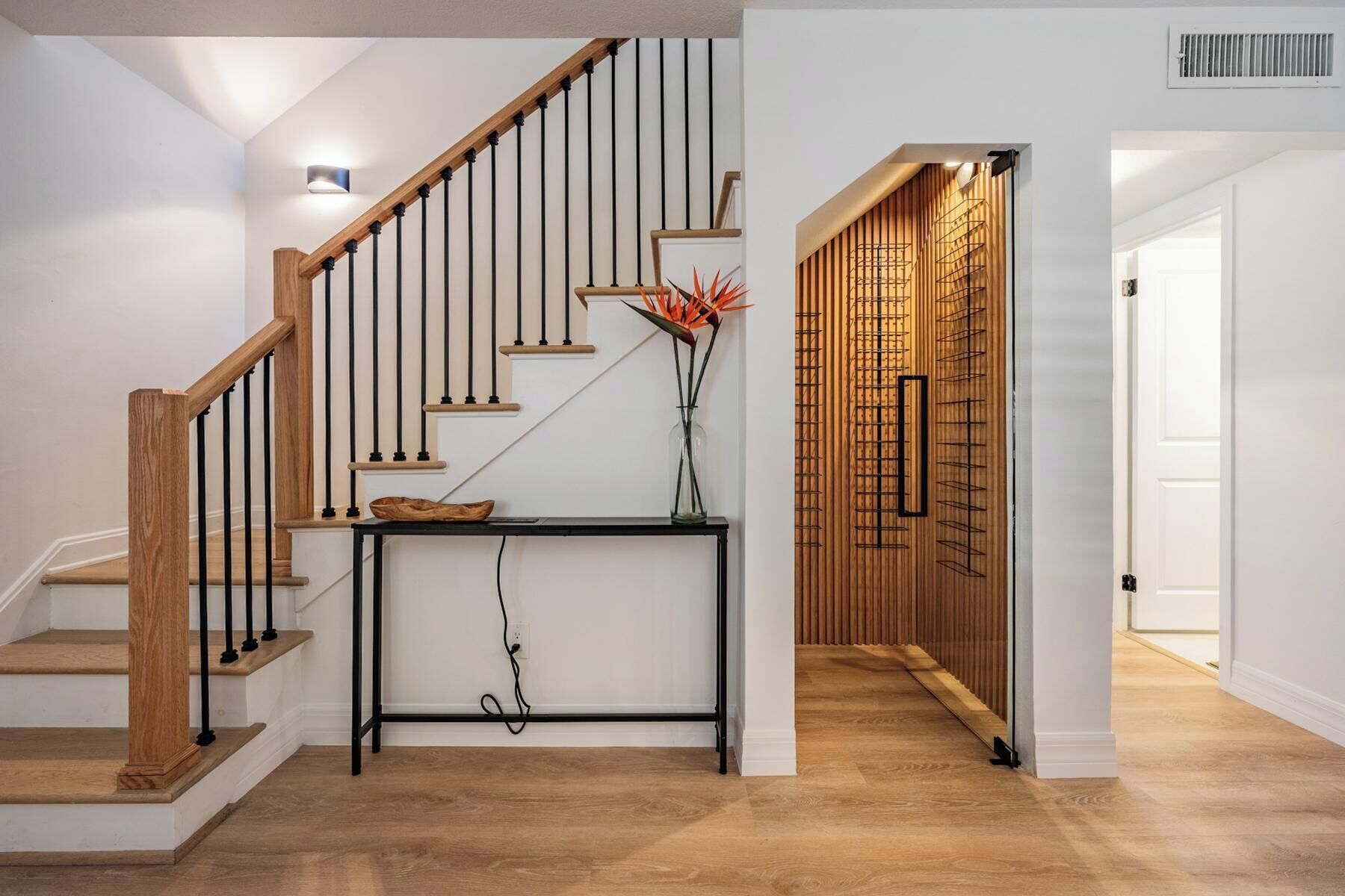 A staircase with wooden steps and black balusters, a console table with a vase and a bowl, and a wall with a bamboo panel design.