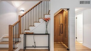 A staircase with wooden steps and black balusters, a console table with a vase and a bowl, and a wall with a bamboo panel design. - Modern Waterfront Home w/ Pool Near Airport & South Tampa Hotspots (Tampa)