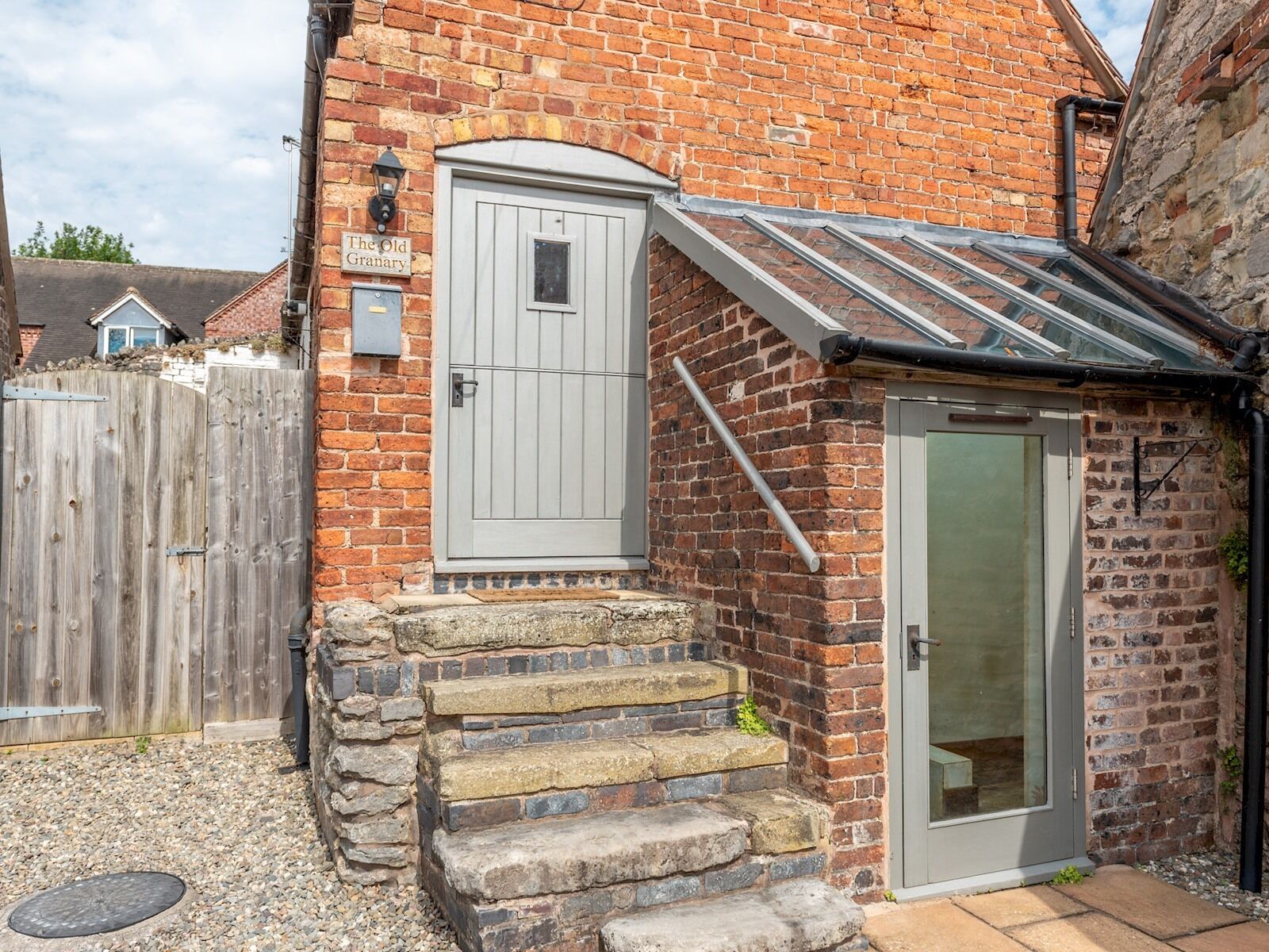 A brick building with a grey door, a small set of stone steps, and a glass door.