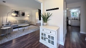 A modern living room with a sofa, coffee table, and a cabinet. There is a hallway leading to a kitchen. - Perfect Location, Minutes to everything Alpharetta & Johns Creek (Alpharetta)