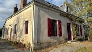 A two-story building with red shutters, a brick chimney, and a gravel driveway.