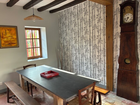A dining area with a wooden table, benches, a red tray, a window with striped curtains, and a wall-mounted clock.