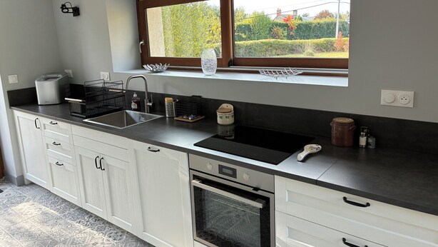 A modern kitchen with a built-in oven, a double sink, and a window with a view of greenery.