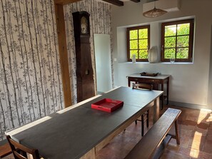 A dining area with a long table, benches, a clock, and two windows with greenery outside. - House (12 people) in Jupilles, between Le Mans and Tours, 28km from the Circuit. (Jupillles)