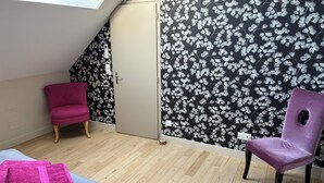 A room with a sloped ceiling, a wardrobe, two chairs, a bed, and a floral wallpaper.