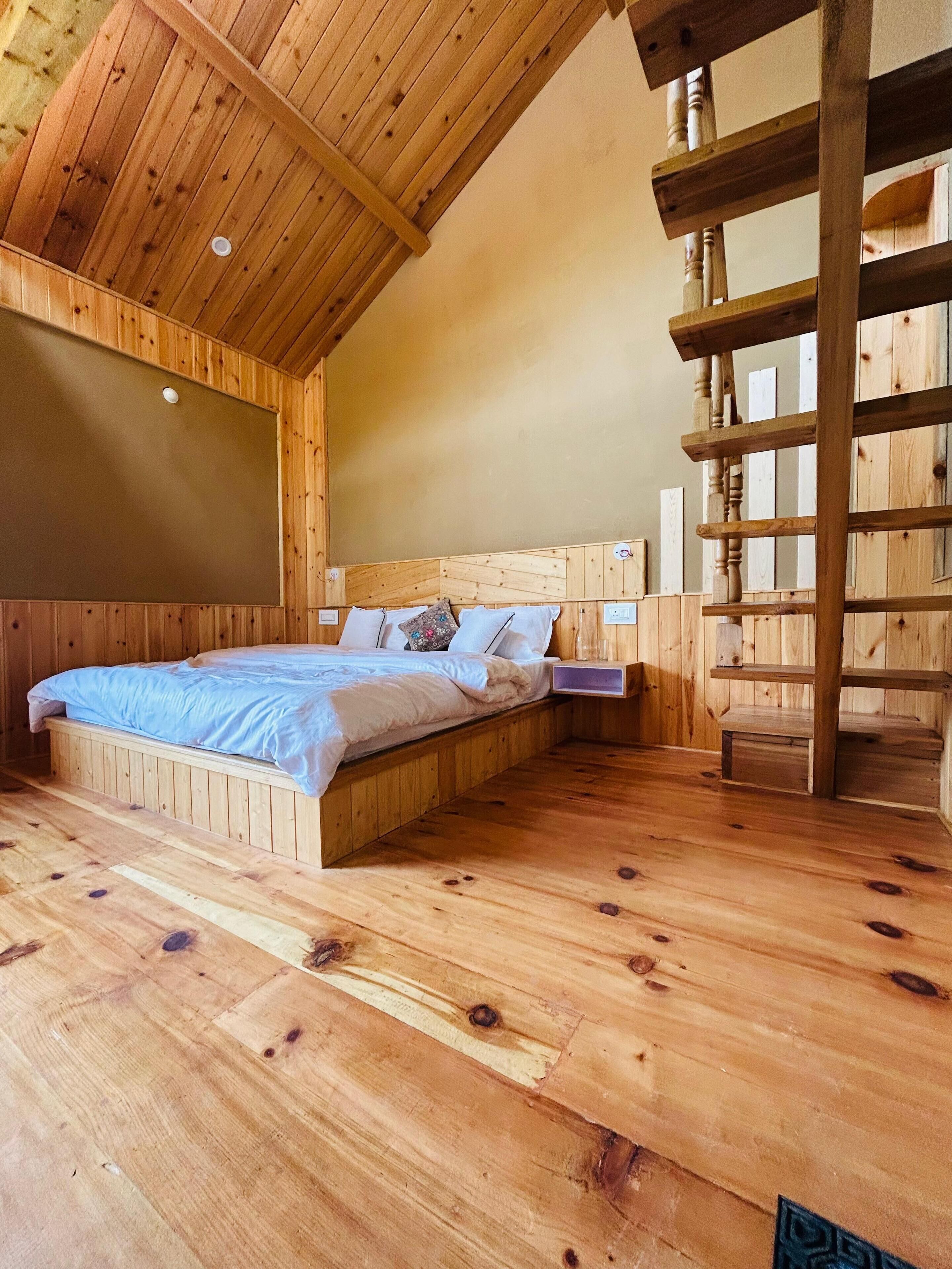 A wooden bedroom with a bunk bed, a wooden ladder, and a sloped ceiling.