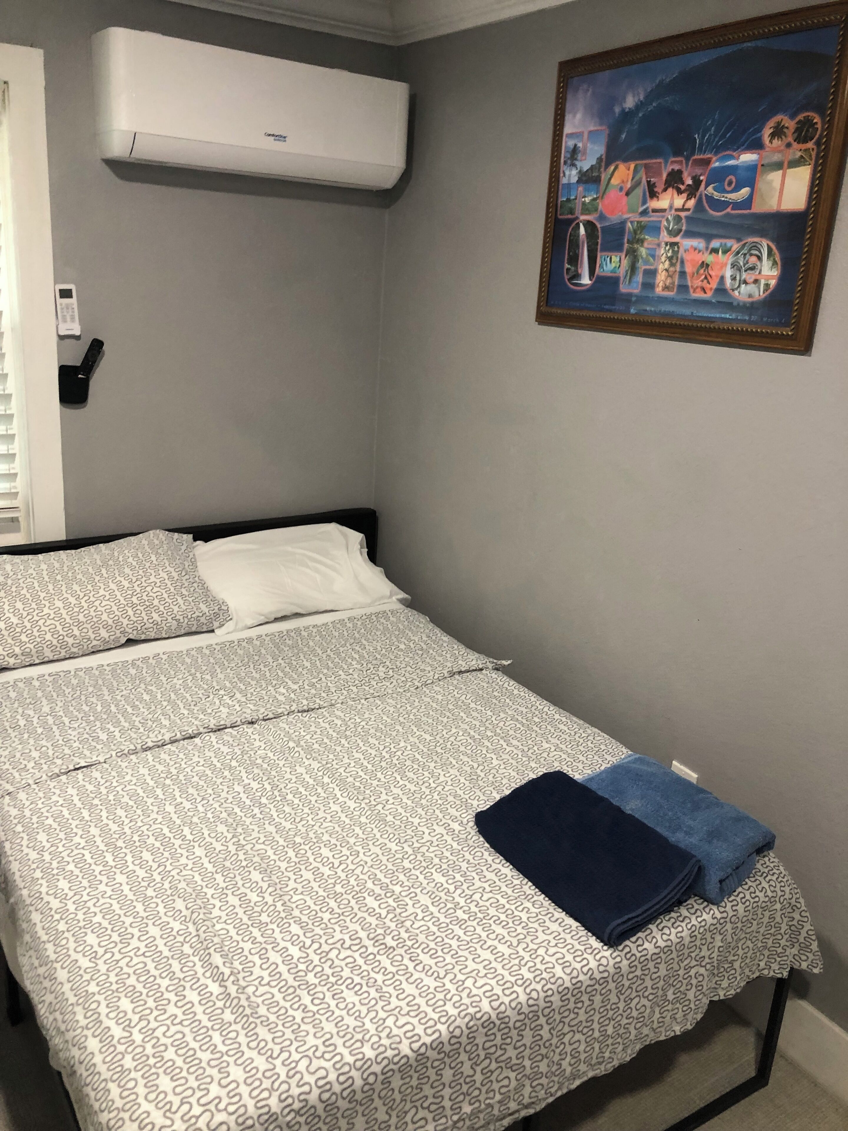 Un dormitorio con cama, aire acondicionado de pared, un cuadro enmarcado y teléfono en la mesita de noche.