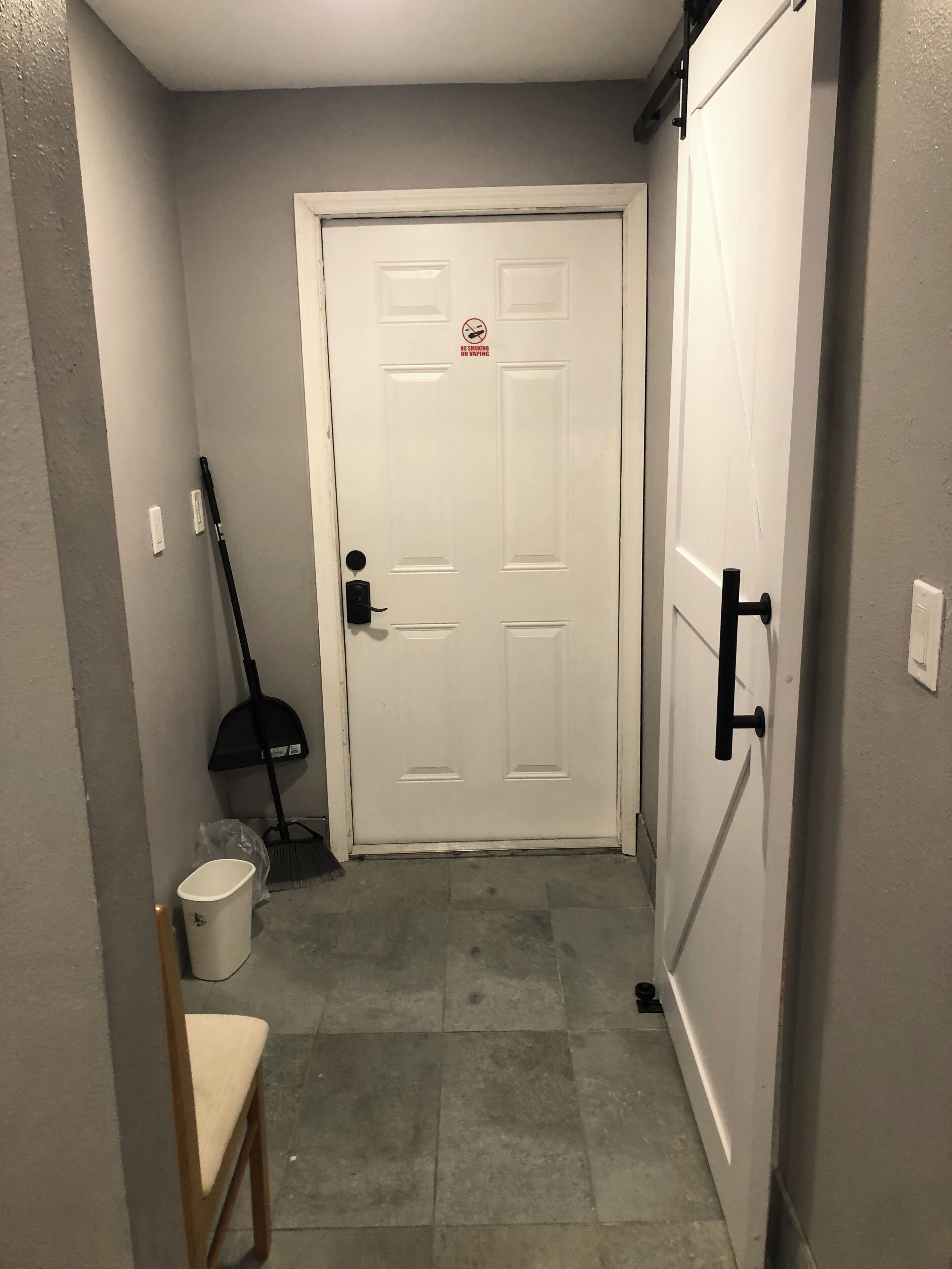 A narrow hallway with a white door, a broom, a dustpan, and a trash bin.