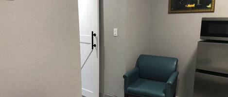 Une pièce avec un fauteuil turquoise, une porte blanche, un réfrigérateur et un tableau accroché au mur.