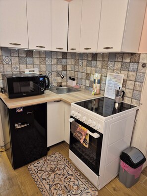 A compact kitchen with a microwave, stove, sink, and a refrigerator. - Cozy 1-bedroom apartment with AC in historic Budapest (Budapest)