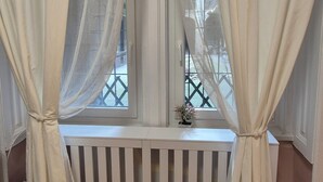 Une pièce avec une fenêtre ornée de rideaux légers, une balustrade blanche et une petite plante en pot posée sur le rebord de la fenêtre.