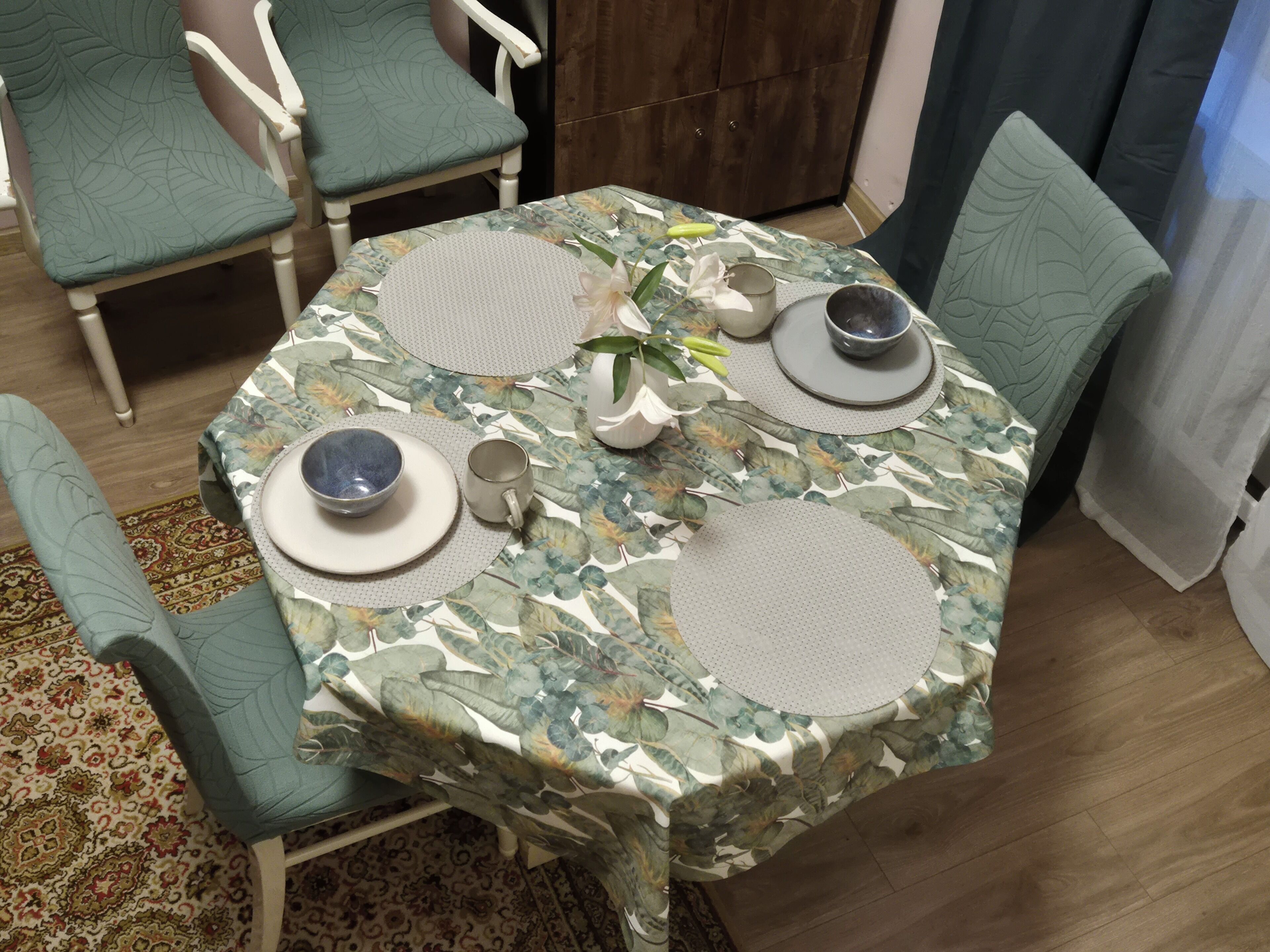 A dining table with a floral tablecloth, surrounded by chairs with a leaf pattern upholstery.