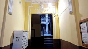 Un couloir orné d’un lustre, avec un escalier et une porte donnant sur une autre pièce.