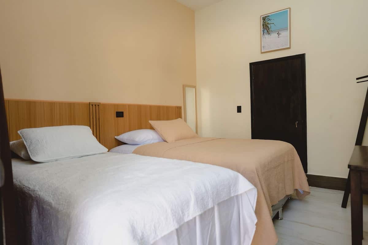 Ein Zimmer mit zwei Betten, einem Holzkopfstück, einer Tür und einem gerahmten Bild an der Wand.