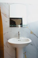 Un baño con un lavamanos blanco de pedestal, un espejo encima y una pared de mármol con vetas amarillas.