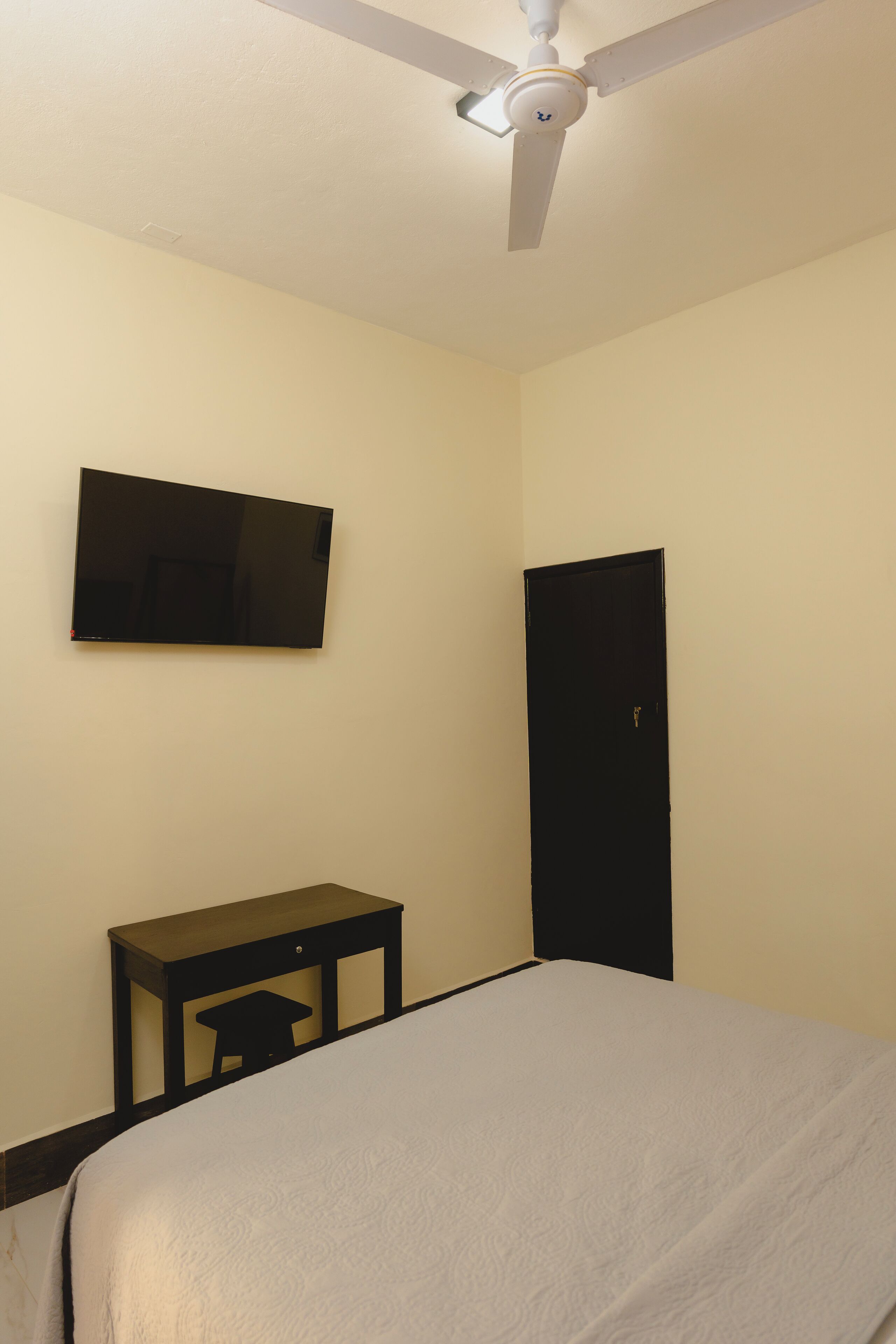 A bedroom with a bed, a desk, a television mounted on the wall, and a door.