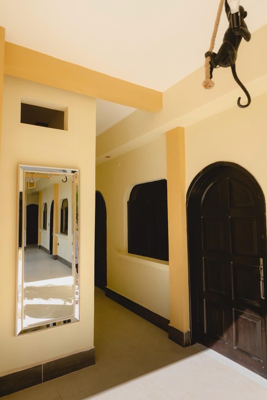 A hallway with a mirror, a black door, and a hanging object.