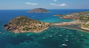 An aerial view of a coastal area with a small island, clear turquoise waters, and numerous boats anchored near the shore. - Modern Sea View Apartment with Balcony (Anavissos)