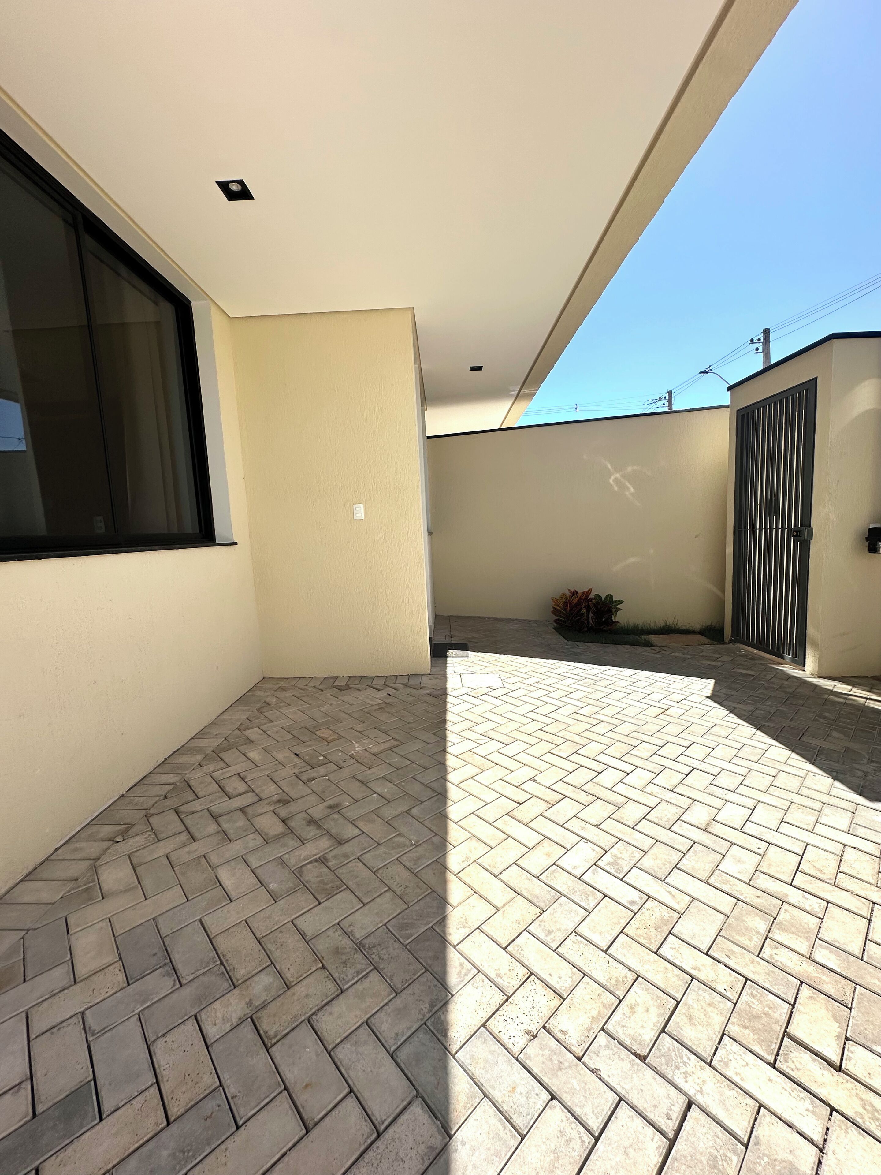A modern outdoor patio area with a herringbone brick floor, a large window, and a metal gate.