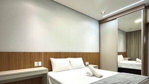 A modern hotel room with a large bed, a wooden headboard, a bedside table, and a mirror. - Apartamento Pequi Luxo com Garagem (Palmas)