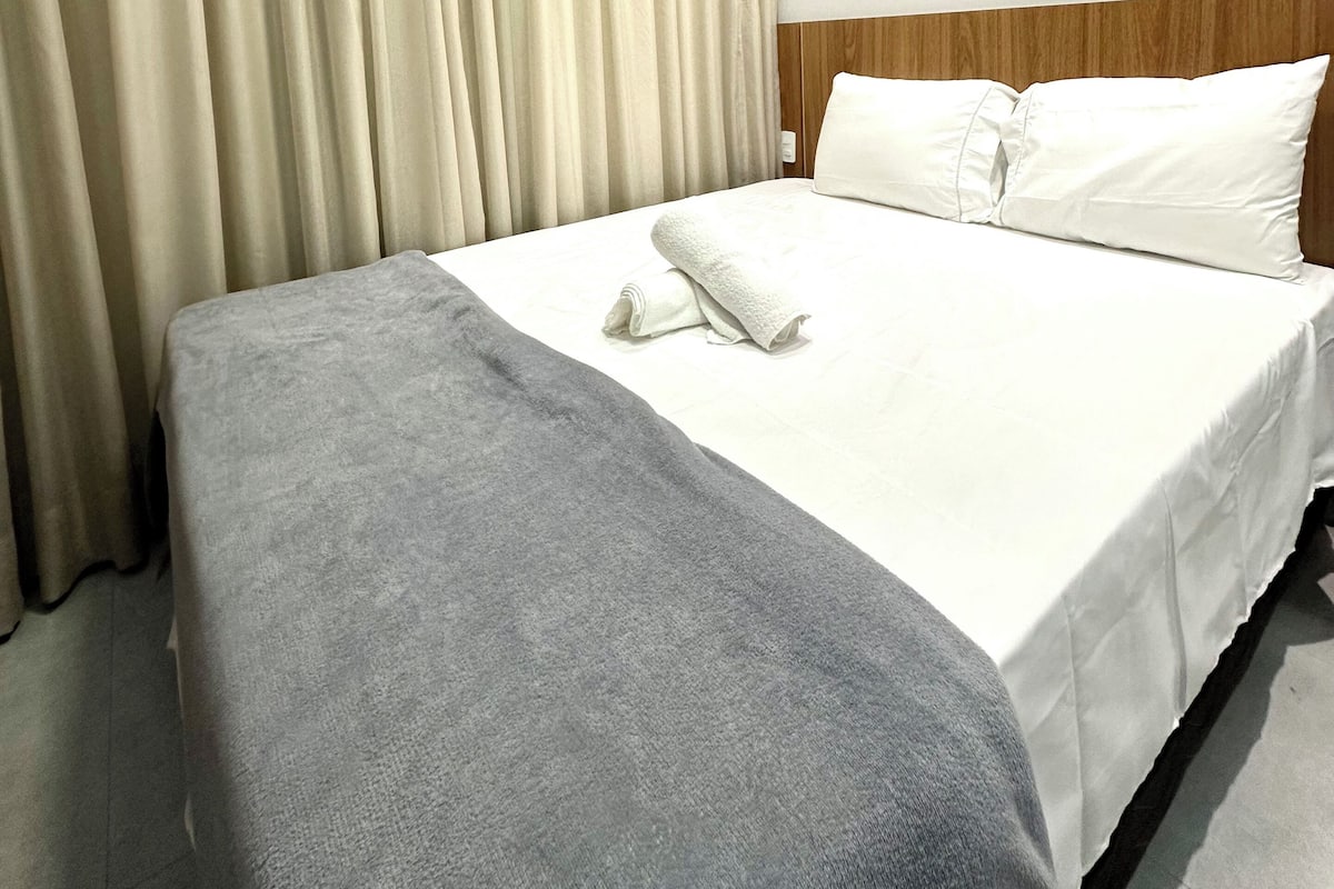 Une chambre d’hôtel avec un lit bien fait, une couverture grise et une tête de lit en bois.