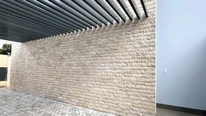 A covered outdoor area with a herringbone-patterned brick floor and a stone wall. - Apartamento Pequi Luxo com Garagem (Palmas)