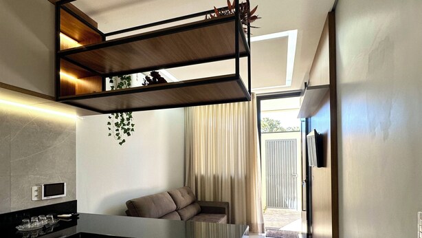 A modern kitchen with a black countertop, a built-in oven, and a dining area with a table and sofa. - Apartamento Pequi Luxo com Garagem (Palmas)