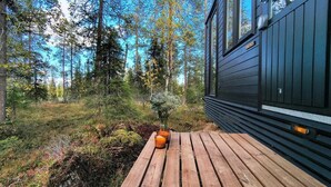 A wooden deck with two candles, surrounded by a forested area and a building with dark siding. - Lapland Fell Village (Sodankyla)