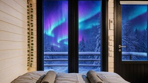 A bedroom with a bed, two rolled towels, and a view of the Northern Lights through a door. - Lapland Fell Village (Sodankyla)