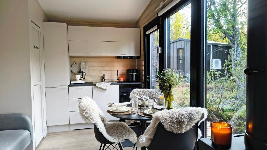 A modern kitchen with white cabinets, a dining area with a table set for two, and a large window offering a view of the outdoors.