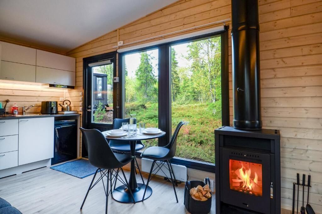 Et moderne køkken med et stort vindue, et spiseområde med stole og en brændeovn.