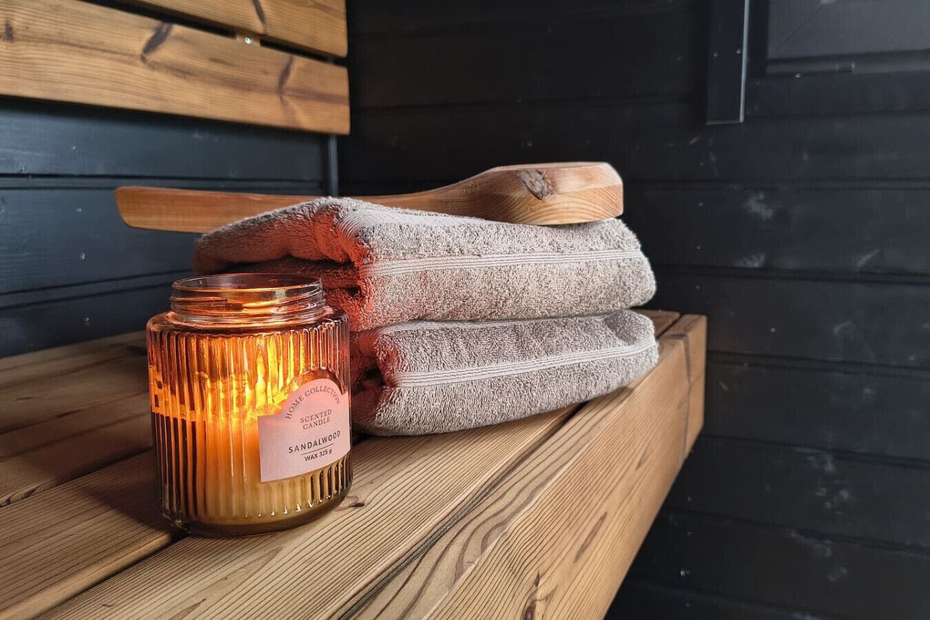 A candle labeled "Sandalwood" on a wooden surface with a wooden spoon and folded towels.