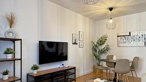 A modern living room with a flat-screen TV, a dining area with a table and chairs, and a large potted plant.
