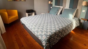 Una camera da letto con un letto, una sedia, un comodino e un quadro appeso al muro.