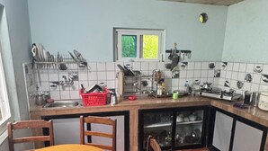 A kitchen with a wooden dining table, chairs, a red basket, and a window with green foliage. - Chipaskot Spot (Pokhara)