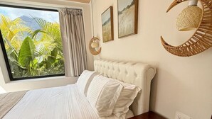 A bedroom with a large window, a bed, a nightstand, and a wall-mounted lamp. - CALALUN (La Fortuna)