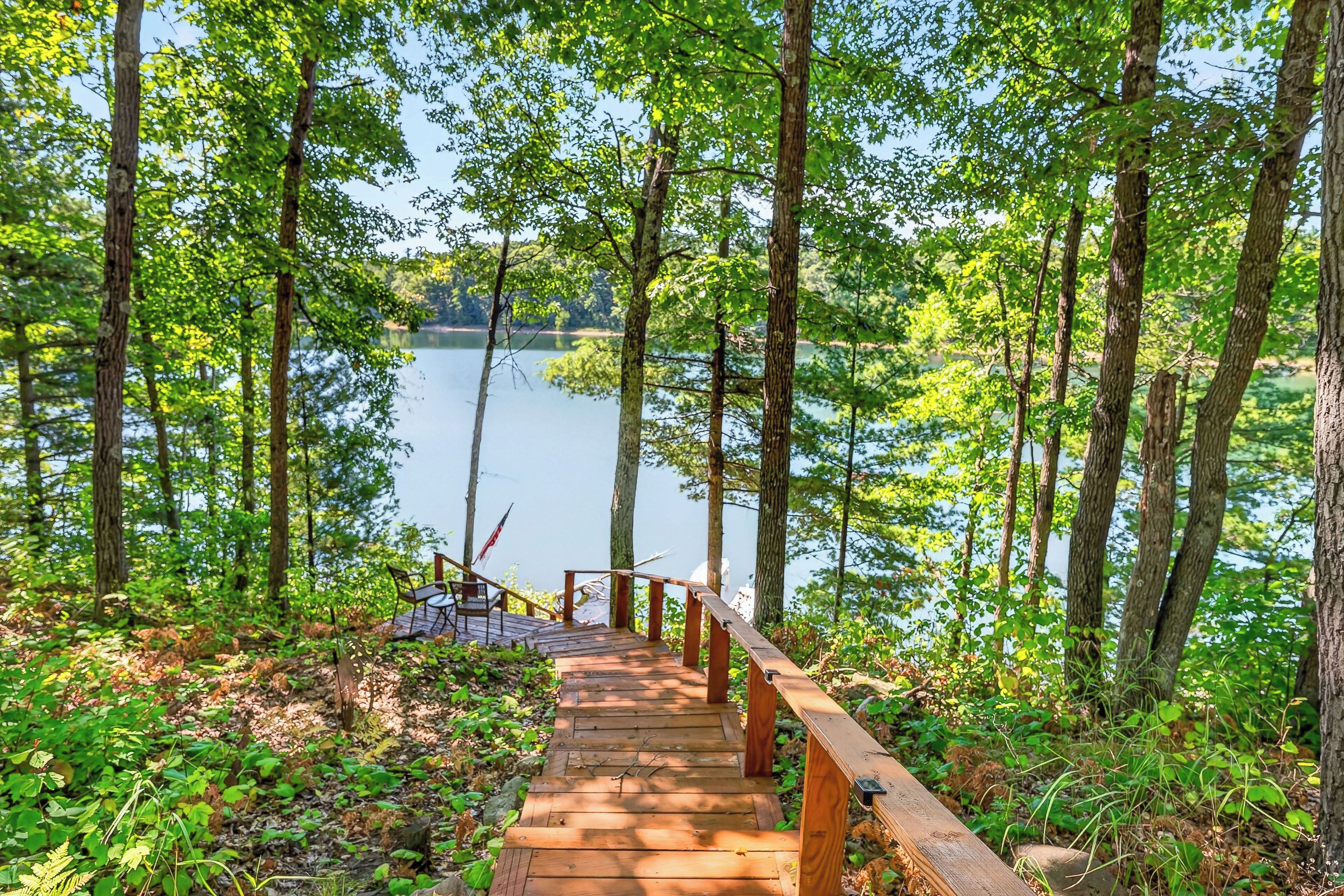 A wooden staircase leading to a dock over a calm lake, surrounded by dense trees.
