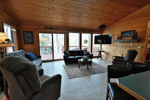 A cozy cabin interior with a wooden ceiling, a fireplace, a television, and a large window overlooking a deck. - Charming 2-bedroom cabin on a private Lake near Stone Lake. (Stone Lake)
