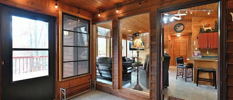 Interior de madera con un divisor de vidrio corredizo que da a una sala de estar, un comedor y una cocina visible a través del divisor, además de una pequeña terraza al aire libre.